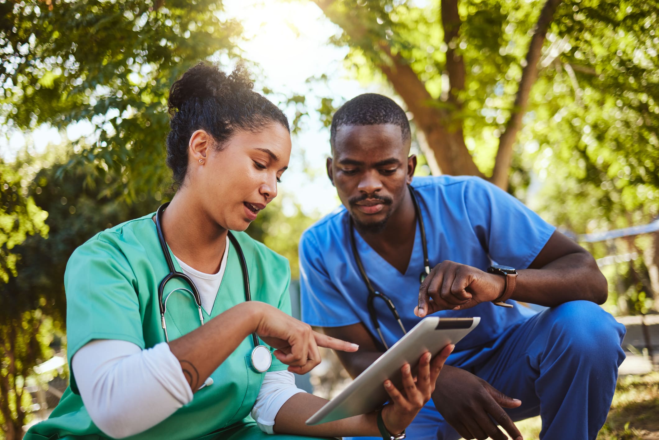Two healthcare professionals reviewing information on a tablet outdoors.