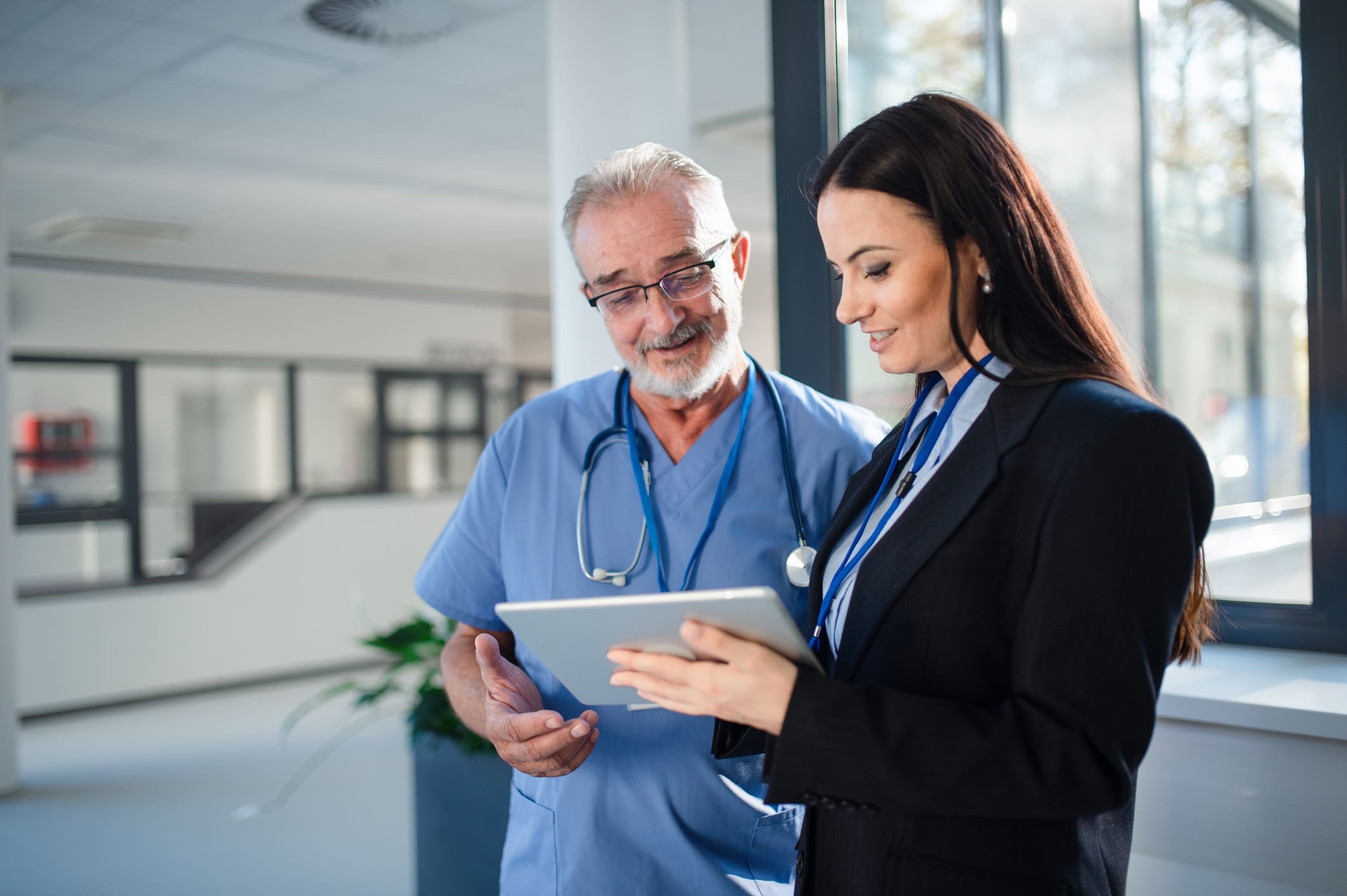A healthcare professional and a businesswoman reviewing information on a tablet.