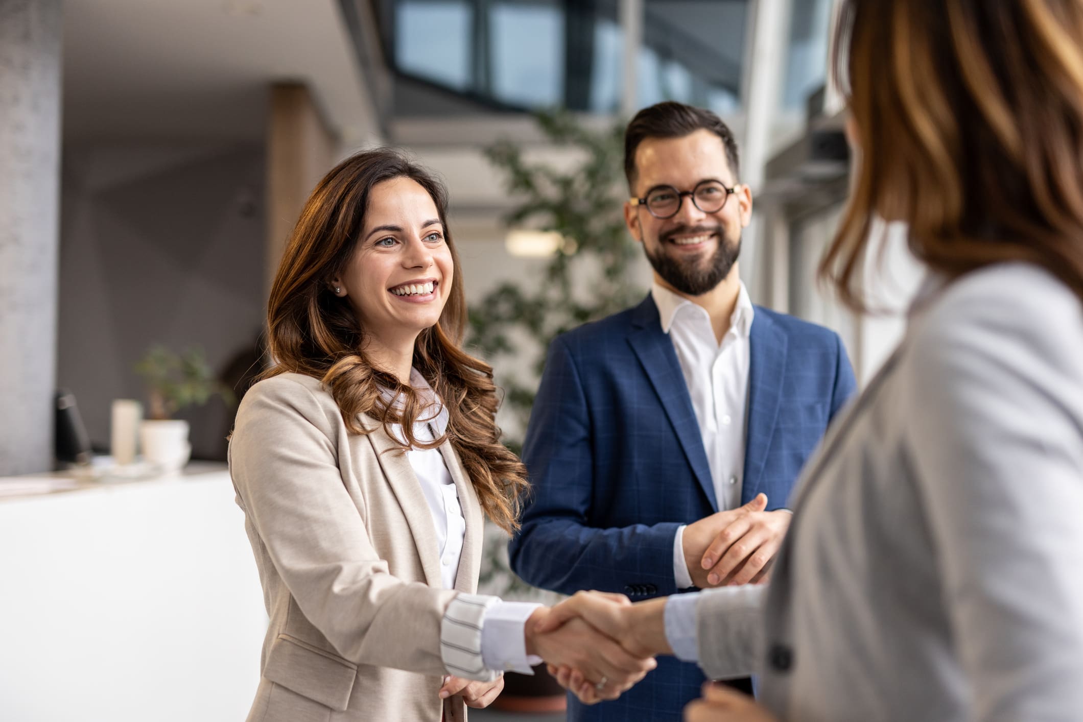Two professionals smiling and shaking hands in a business setting.